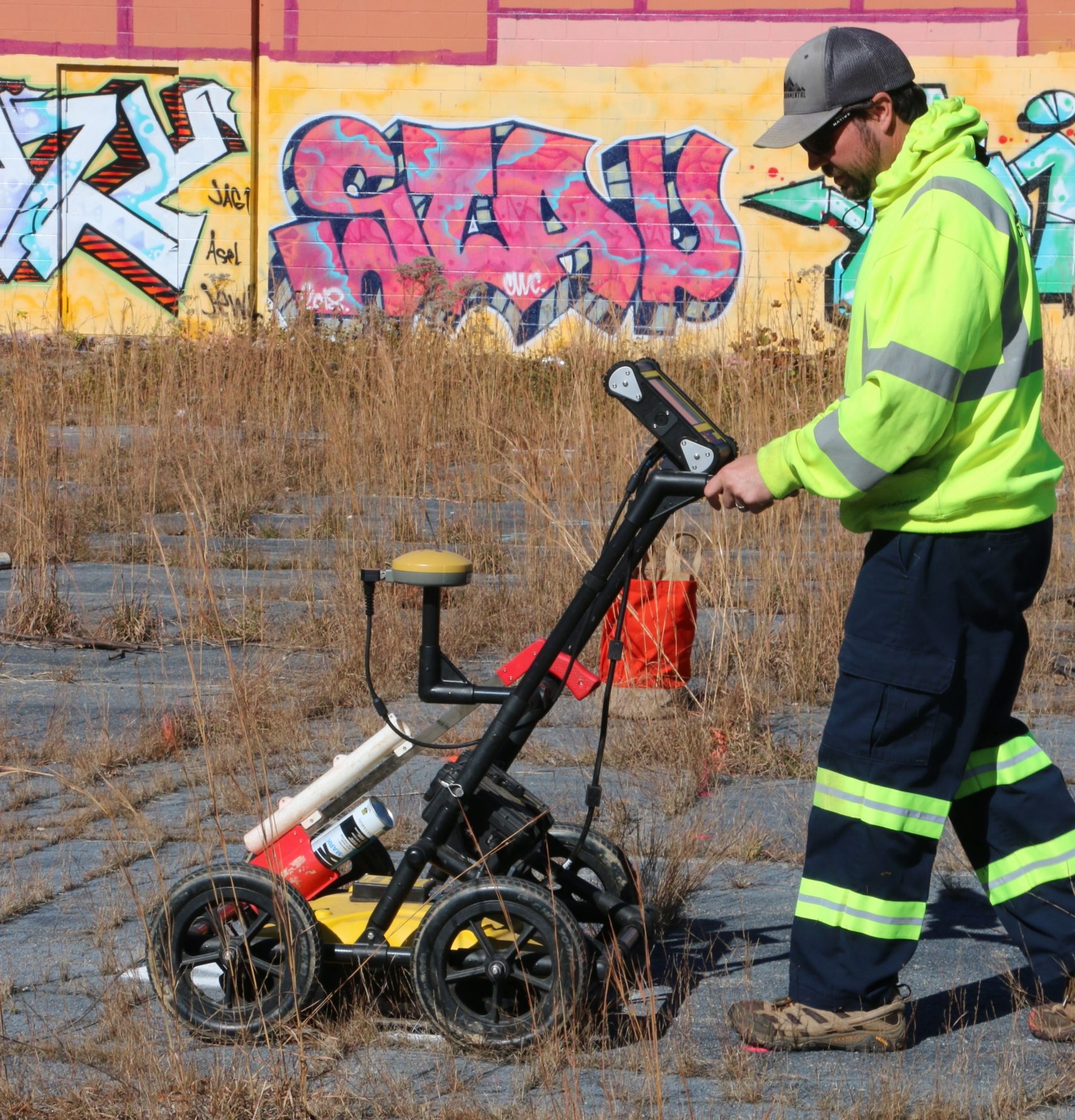 Technician using GPR for borehole clearance at abandoned industrial site - graffiti in background