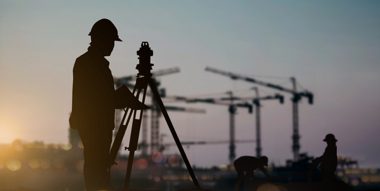 silhouette of surveyor with cranes in background