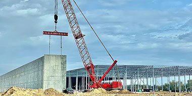 Red crane with industrial construction site in background.